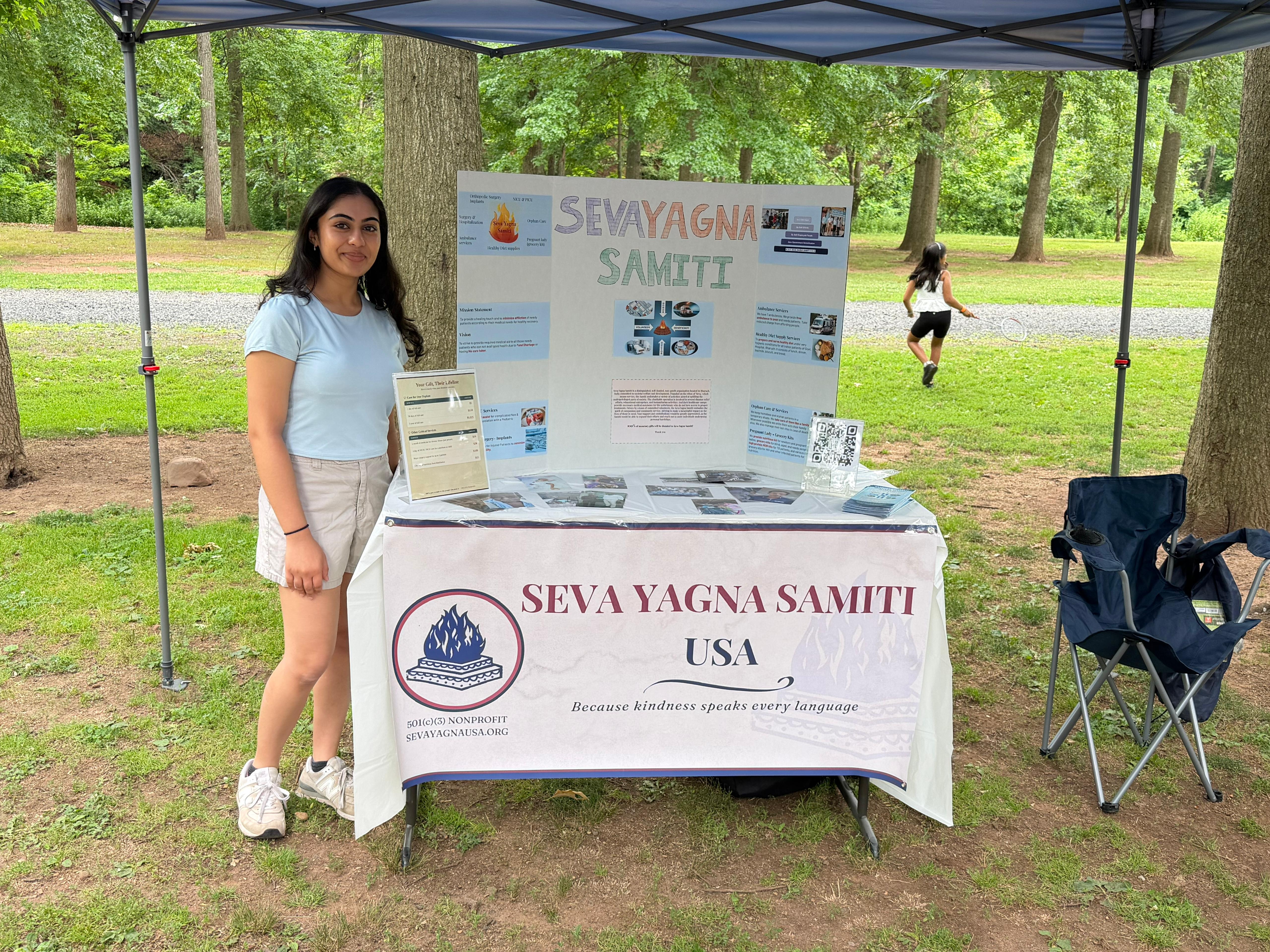 A Seva Yagna Samiti USA volunteer at the organization's outreach table with informational displays